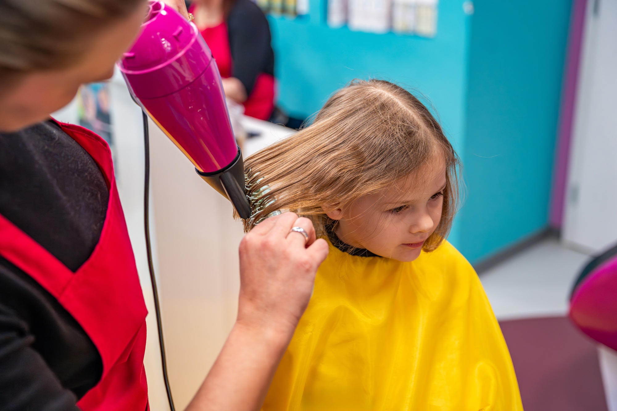 Hairdresser making a hair style to cute little girl in real child salon with colorful interior and